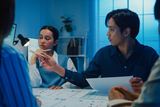 Asia businesspeople presentation sales meeting plan statistics brainstorm and work with paperwork around table in office conference room at night. Business finance partner strategy investment success.