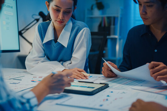 Startup Asia businesspeople meeting plan analysis statistics brainstorm and tablet point graph chart employee take note in office conference room at night. Business finance partners strategy success.