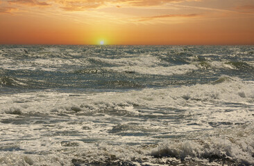 Obraz premium Golden sunset over a choppy ocean with waves crashing and foam