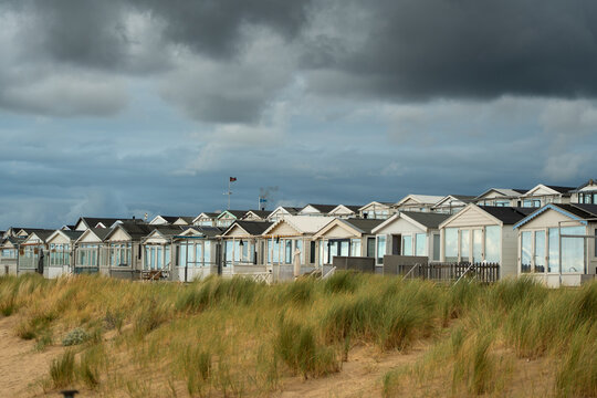 View of beach houses at the Kleine Strand with wind turbines and the Tata Steel industrial complex in the background under a cloudy sky in IJmuiden, North Holland, Netherlands.