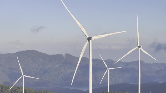 Aerial drone view of Cau Dat tea hills and wind turbines at sunset in Xuan Truong, Da Lat, Lam Dong, Vietnam, showcasing renewable energy and scenic highland landscapes.