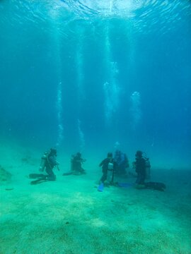 View of scuba divers kneeling on the sandy seabed with air bubbles rising to the surface in the clear blue water in Kas, Antalya, Turkey.