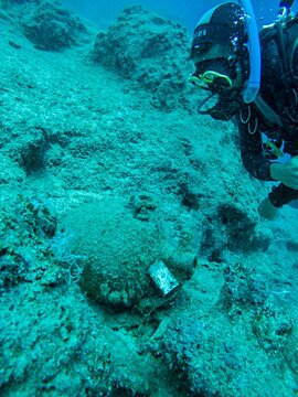 View of a scuba diver exploring an ancient underwater archaeological site with a submerged amphora and clear blue water in Kas, Antalya, Turkey.