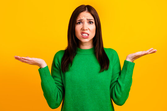 Confused woman shrugging in green sweater against bright yellow background with puzzled expression and questioning gesture conveying uncertainty, doubt and nonverbal communication concepts