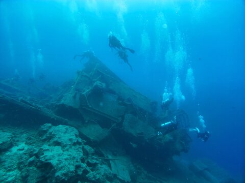 View of scuba divers exploring a sunken shipwreck in the deep blue sea with bubbles rising to the surface in Kas, Antalya, Turkey.