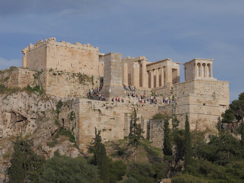 View of the ancient Acropolis of Athens with its historic columns, stone ruins, and visitors walking along the steps under a clear blue sky in Athens, Greece.