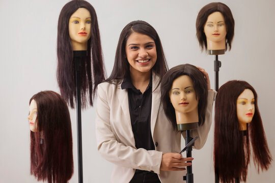 A YOUNG HAIR STYLIST HAPPILY POSING WITH DUMMY HAIR