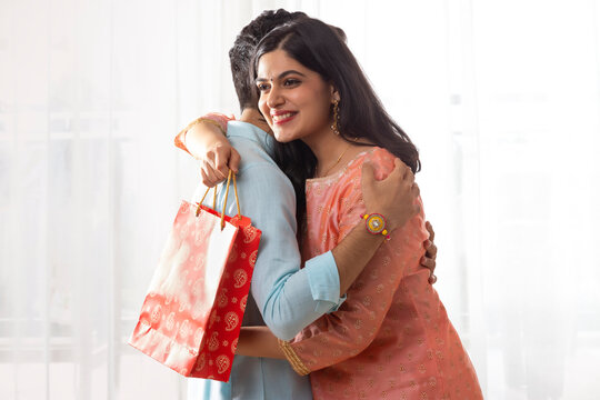 A HAPPY YOUNG WOMAN EMBRACING BROTHER WHILE HOLDING GIFT