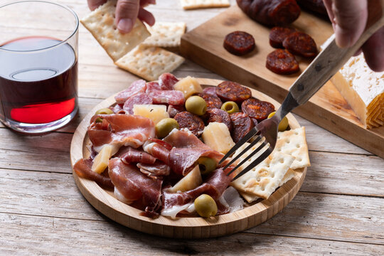 Fork picking up serrano ham from Spanish charcuterie board on wooden table