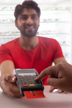 A HAPPY YOUNG MAN HOLDING CARD MACHINE FOR CUSTOMER TO PAY BILL