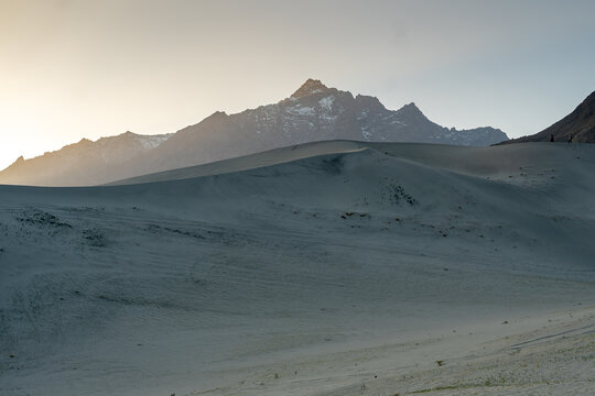 View of the Sarfaranga Cold Desert Shigar with vast sand dunes and snow-capped mountains in the background under a soft morning light in Skardu, Gilgit, Pakistan.