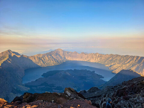 View of the volcanic crater and Segara Anak lake from the peak of Mount Rinjani with rocky terrain under a clear sky in Sembalun, West Nusa Tenggara, Indonesia.