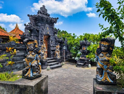 View of the entrance to Tanah Lot temple featuring traditional Balinese guardian statues, intricate black stone carvings, and lush greenery in Kediri, Bali, Indonesia.