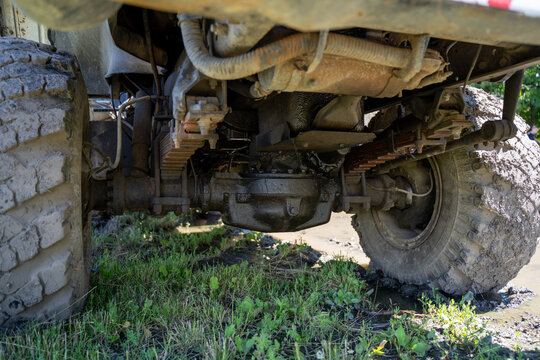 Undercarriage view of heavy truck with dirty axle, leaf spring suspension, and muddy wheels on off-road terrain during daytime.