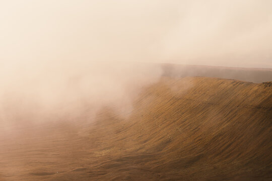 View of the misty slopes of Bannau Brycheiniog National Park with golden grasses and rolling hills in Brecon, Wales, United Kingdom.