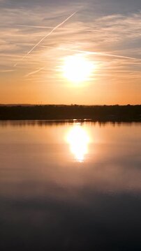 Sunset aerial panorama over Mittellandkanal in Saxony-Anhalt, Germany, with glowing water winding through flat countryside. Warm evening light reveals farmland, forest, horizon and distant turbines