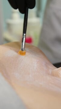 Professional beautician applying cleansing mask on female client's face. Close-up of female face during youth restoration and facial rejuvenation procedure  - Vertical Video