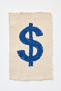 Hand-painted blue dollar sign on rough natural canvas fabric, conceptual image of money, finance and handmade creativity