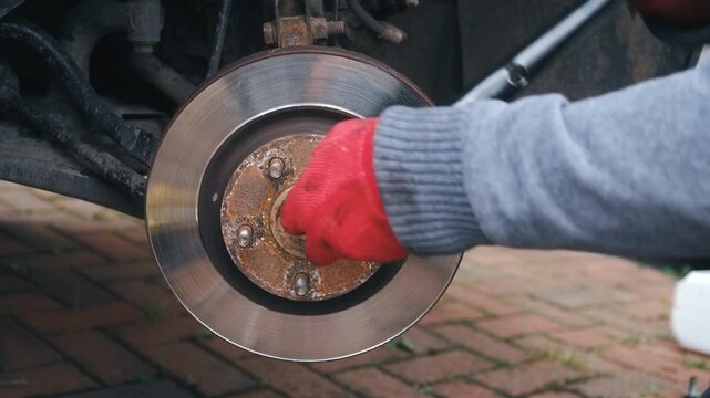 Mechanic tightening puller tool to remove seized brake disc from wheel hub. Automotive repair extracting stuck brake rotor during car maintenance with manual equipment. Closeup loosening corroded