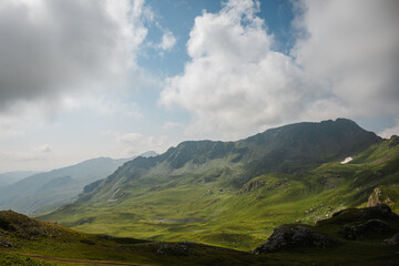 Fototapeta premium Green mountain ridge beneath dramatic white clouds and blue sky