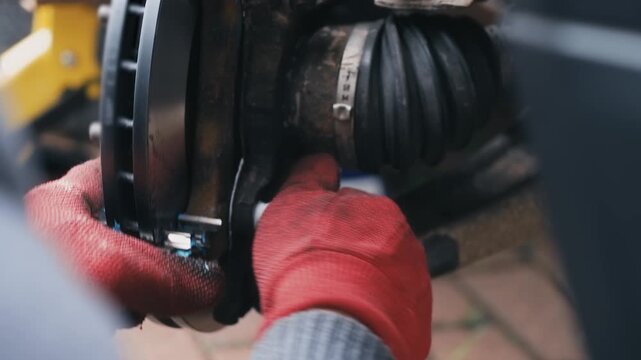 Mechanic tightening brake caliper bolts during car repair. Close up automotive brake disc and axle maintenance with protective gloves. Vehicle system repair process industrial transportation
