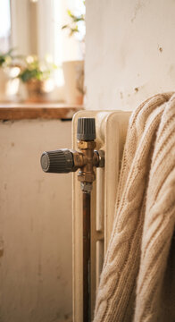 Radiator valve close up with thick knitted blanket beside a pale wall and window light, showing cozy home heating detail