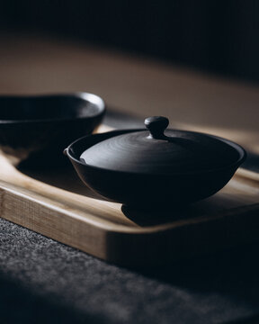 View of a dark matte ceramic teapot with a lid resting on a wooden tray in a minimalist setting in CZ.
