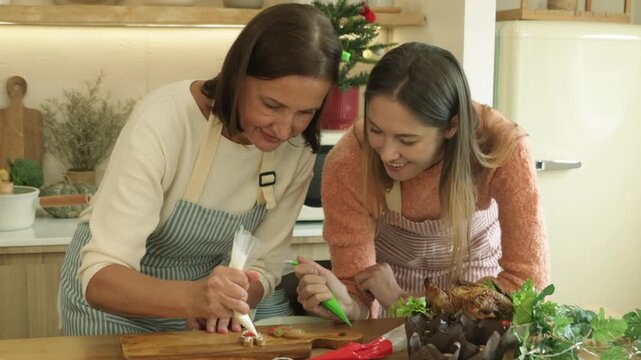 Mother and her grown up daughter are preparing icing decorations for baked cookies on the kitchen counter getting ready for Thanksgiving and family Christmas party.