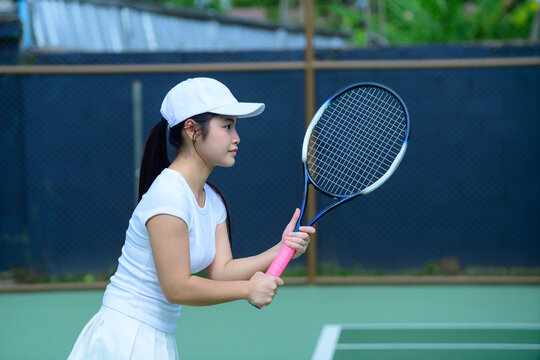 Young Asian Woman Playing Tennis on Outdoor Court in White Sportswear Holding Racket Ready Position