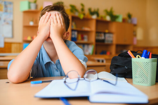 Schoolboy covering face, experiencing bullying and stress in classroom