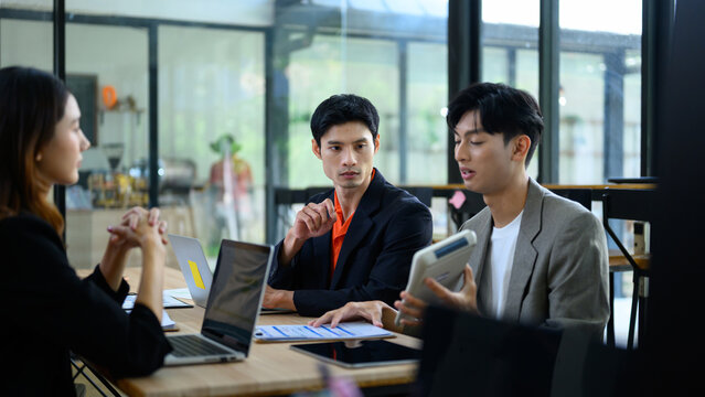 Asian Business Team Having Serious Discussion with Tablet and Laptop in Modern Office Meeting