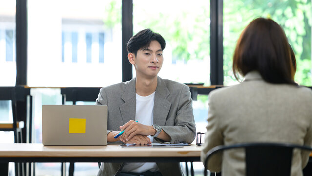 Young Asian Man Conducting a Job Interview with Female Candidate at Office Desk with Laptop