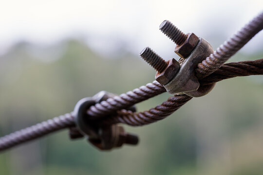 weathered steel wire rope secured with a rusted metal clamp and threaded bolts, highlighting industrial hardware, corrosion, texture, and mechanical detail against a soft blurred background