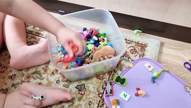 
A small autistic child puts small toys into a box with his hands