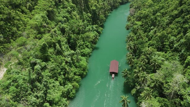Top-down drone follows a Loboc River cruise boat, then tilts up to reveal the green river and forested mountains of Bohol