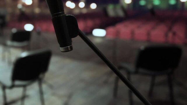 A microphone is set up on stage in a theater. There are several empty chairs arranged in rows in the background. The setting is quiet and ready for an event.
