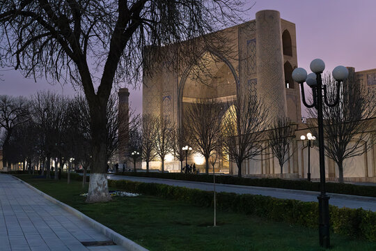 Bibi Khanym Mosque illuminated at twilight in Samarkand with bare winter trees and manicured gardens in the foreground. Ideal for travel publications, tourism brochures, and cultural heritage content.