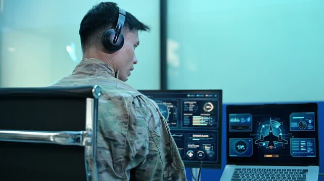 Military operator with headset analyzes radar HUD screens and takes notes in high tech command center, ensuring strategic cyber
