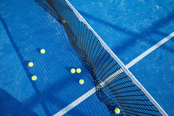 Naklejka premium Aerial top down view of a black tennis net and yellow balls scattered on a vibrant blue artificial turf court