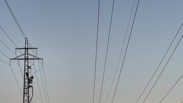 series of lattice transmission towers and utility poles linked by parallel power lines across flat rural field toward horizon, creating calm geometric pattern at