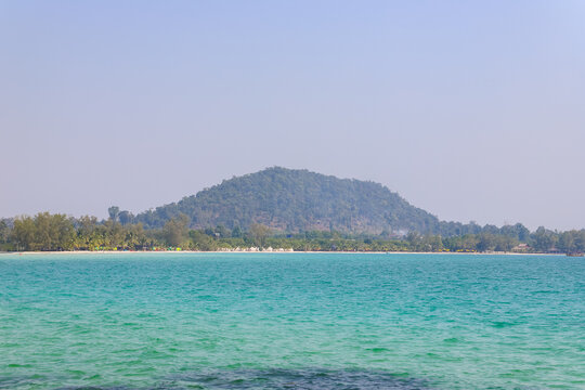View of the tropical coastline of Koh Rong Sanloem with turquoise waters, a sandy beach, and a forested hill in the background in Preah Sihanouk, Sihanoukville, Cambodia.