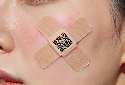Close‑up artistic shot of a cheek with two crossed bandages and a printed QR code, blending medical symbolism with digital identity in a minimal, modern composition.