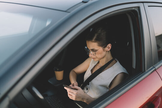 Woman using a smartphone while sitting in the front seat of a parked car
