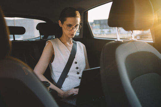 Businesswoman working on laptop in back seat of car