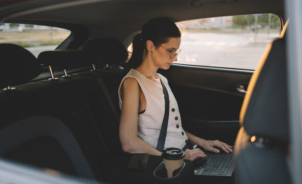 Businesswoman working on laptop in back seat of car