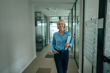Fototapeta premium Businesswoman walking in modern office corridor holding laptop