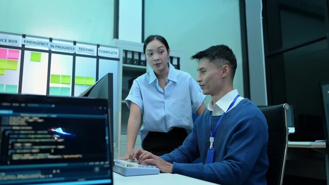 Two Asian software developers collaborating, discussing source code on screen, and troubleshooting