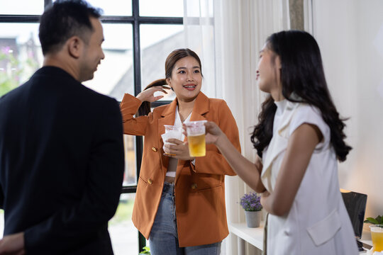 Coworkers drinking and talking during office party. Asian business people enjoying drinks and conversation during a casual office party, fostering team building and celebrating success.