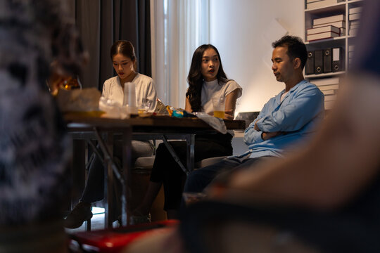 Asian friends enjoying a house party, sharing drinks and snacks at a table. Celebrating friendship and togetherness.