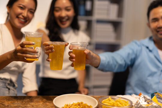 Friends toasting drinks celebrating success at office party. Group of happy young Asian business colleagues toasting with beer and juice, enjoying office celebration.